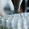 Close-up of a machine dispensing liquid into clear glass bottles on an assembly line.