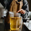 Person pouring hot wax from a spoon into a measuring cup